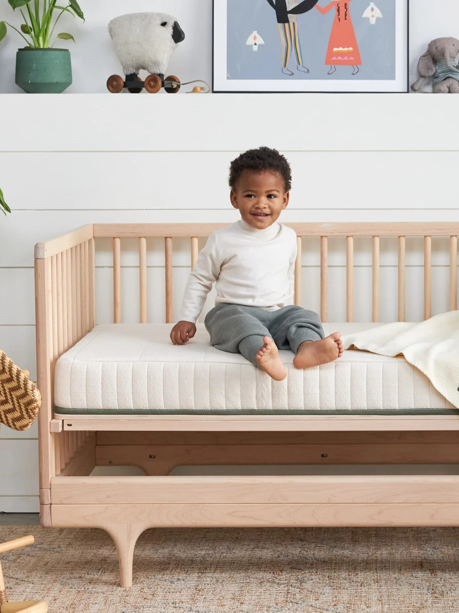 A young child sits on a mattress in a crib