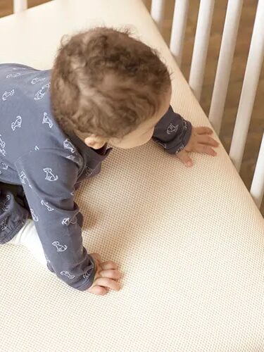 A baby crawls to the edge of a mattress in a crib