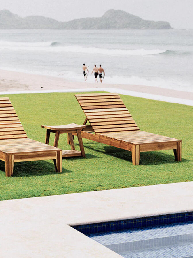 Two wooden loungers with side table on a lawn near the beach