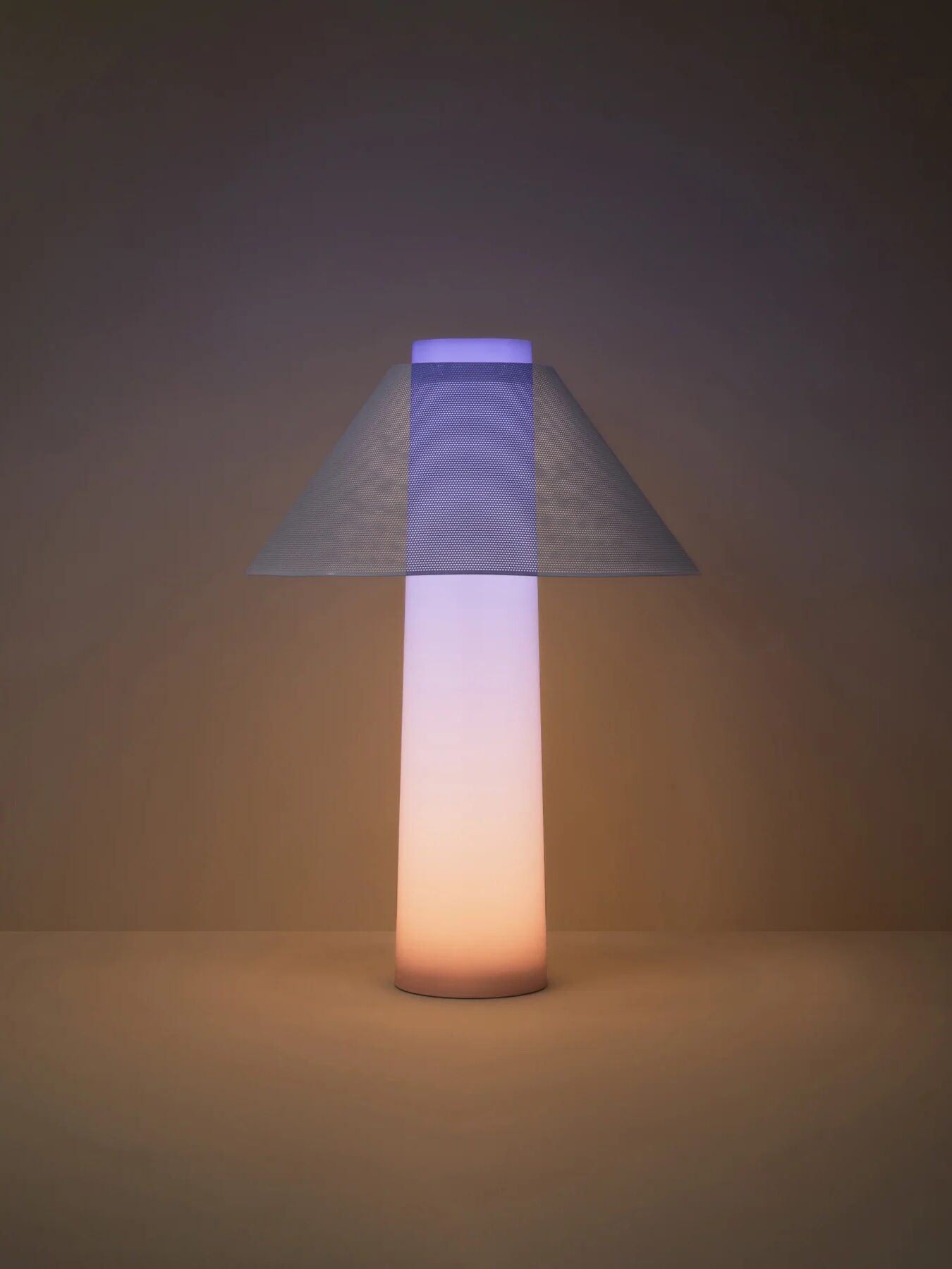 Loftie lamp in a soft light mode sits on the table, its base a warm light and the top a blue light.