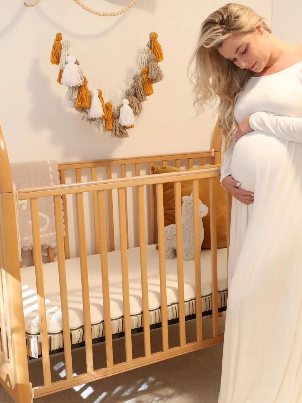 A pregnant woman cradles her belly next to a crib
