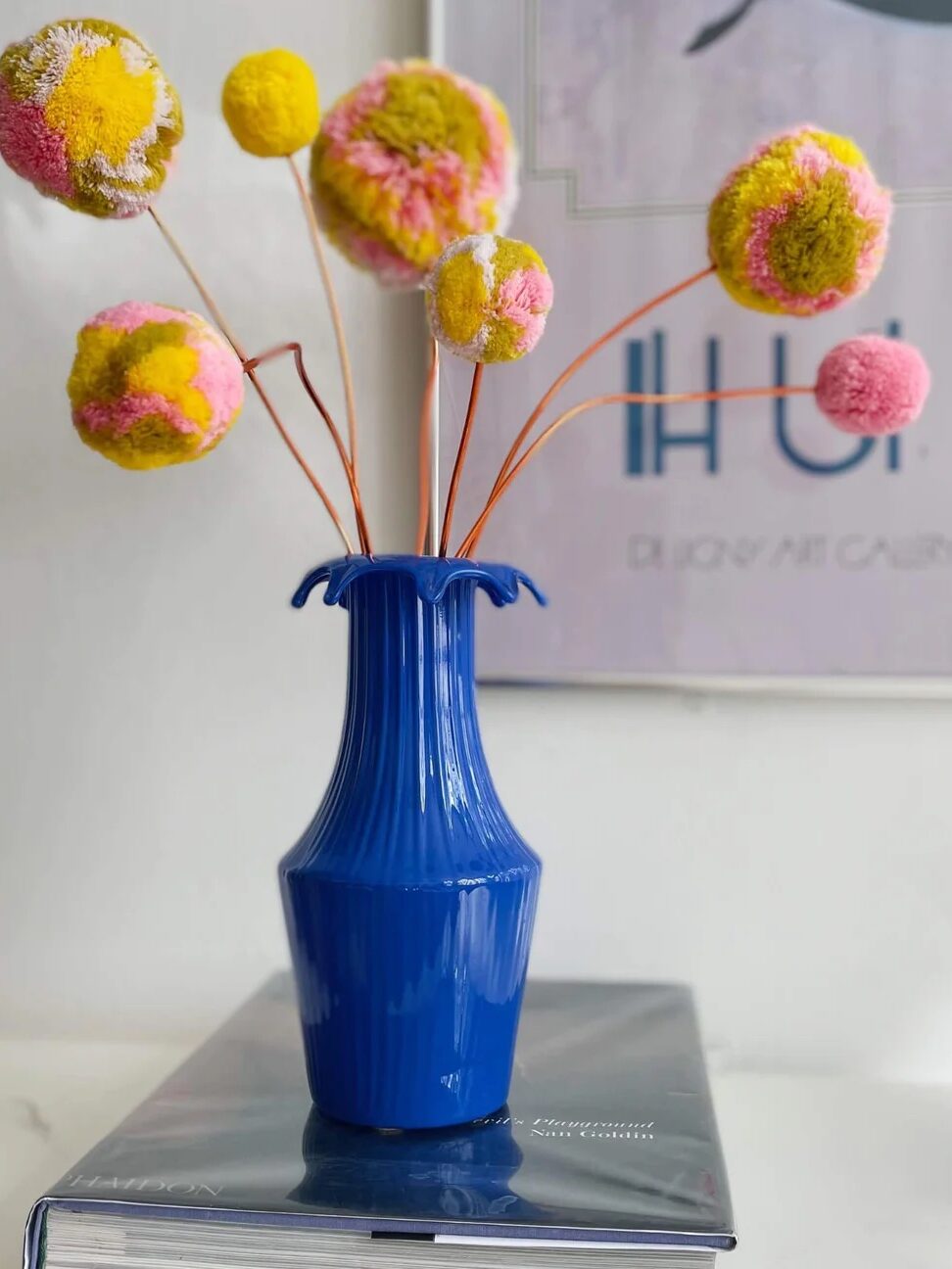 Seven yellow and pink pom stems sit in a blue vase on a table