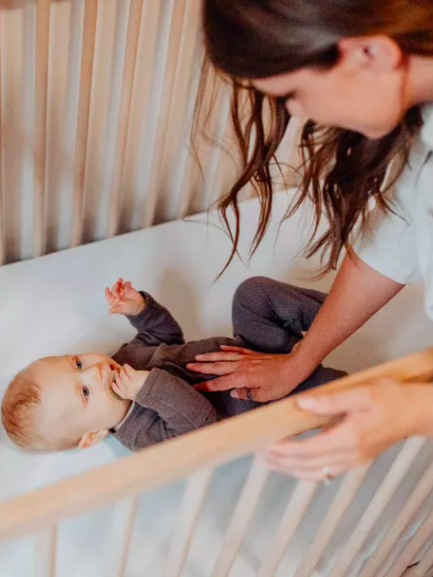 A woman bends over a crib and puts her hand on a baby's belly